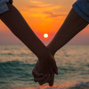 Two people holding hands at sunset on the beach.